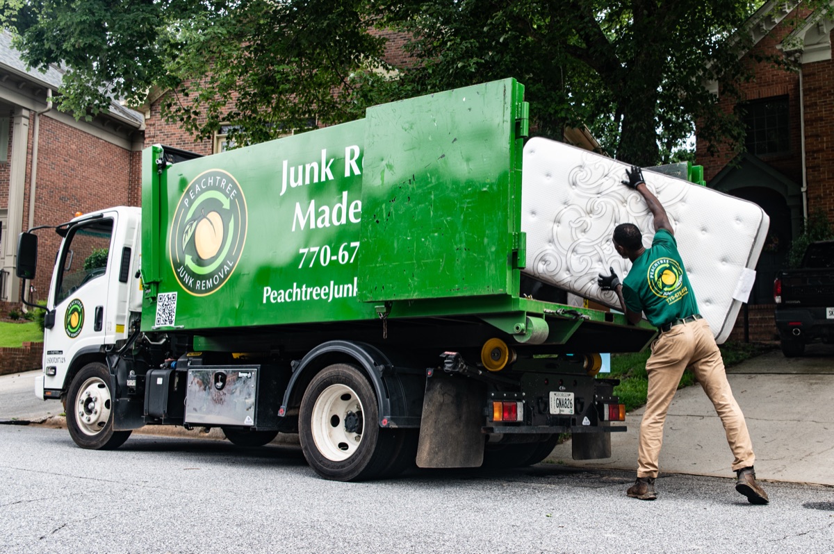 A uniformed Peachtree crew member heaving a mattress into the truck
